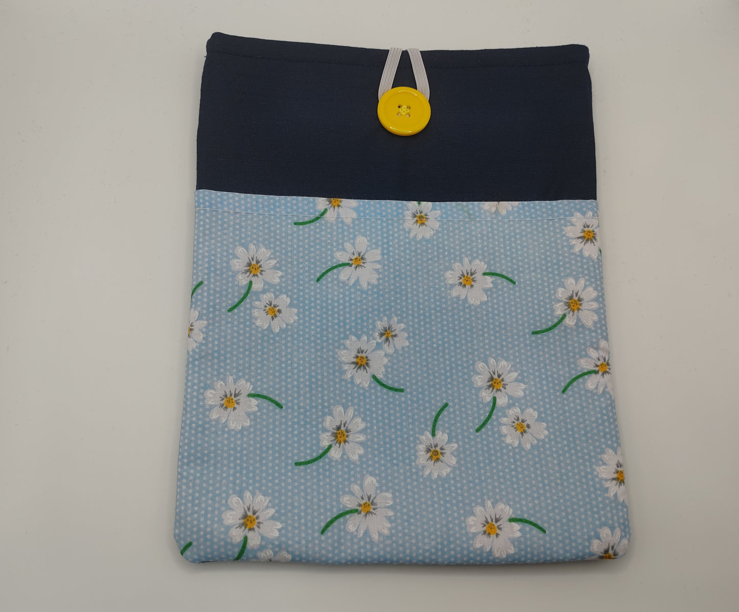 A blue floral book sleeve with a front pocket, designed to fit a standard paperback book. It features a button and elastic clasp for securing the book.